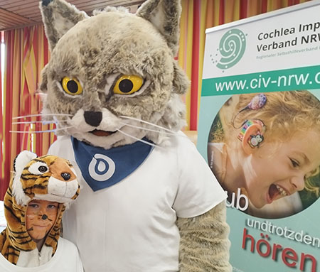Person im Luchskostüm, an der Seite Kind im Kostüm, im Hintergrund RollUp des CIV NRW